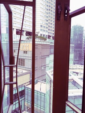A view through a window with a metal frame, overlooking a cityscape with modern buildings and a sign reading 'K11'. - Wing Lee Guest House (Hong Kong)