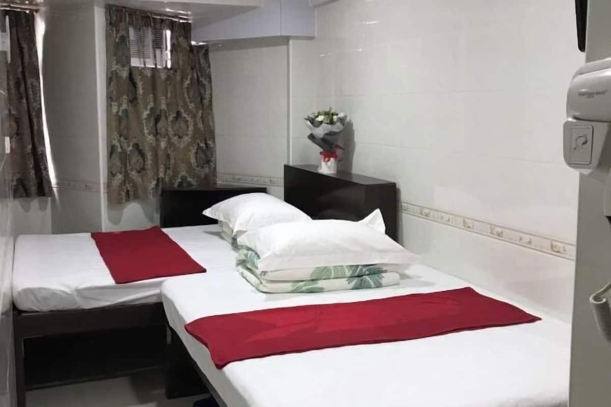 A hotel room with two beds, a nightstand, a vase with flowers, and a window with curtains.