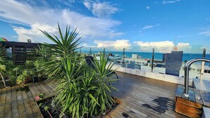 Eine Dachterrasse mit Meerblick, ausgestattet mit einem Holzboden, Topfpflanzen und einem Metallgeländer.
