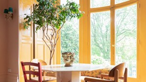 A dining area with a marble table, two wooden chairs, a potted plant, and a view through large windows. - Belsize Park Gardens by onefinestay (London)