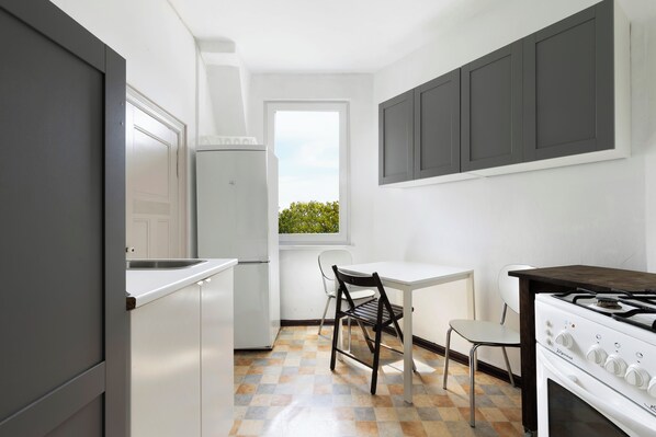 Una cocina compacta con un refrigerador blanco, una estufa a gas, una ventana con vista a la vegetación y un piso de baldosas.
