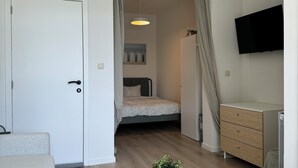 Una habitación moderna y bien iluminada con una cama, un televisor montado en la pared, una mesa de centro de madera con una planta y una vela, y un aparador.
