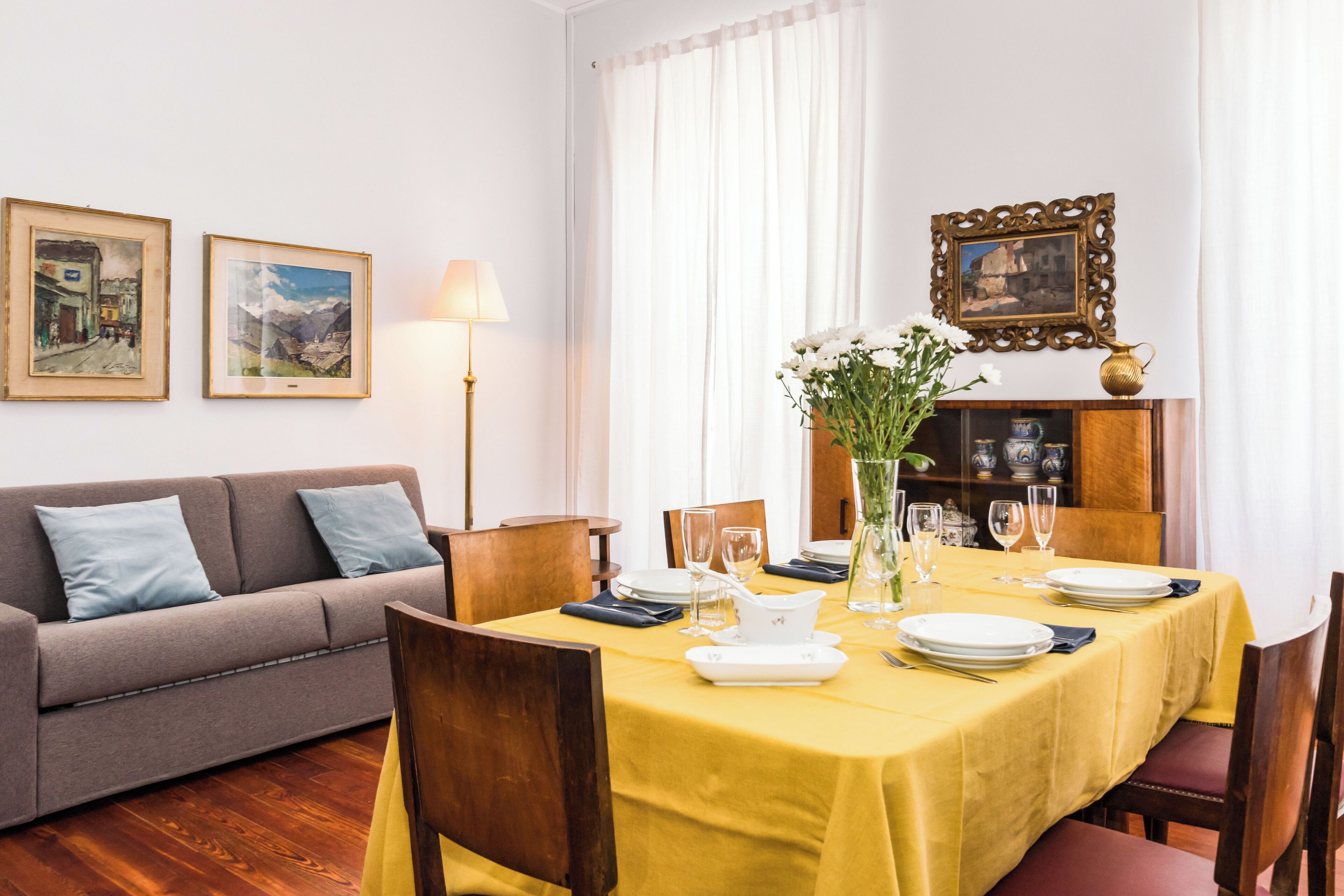 A dining area with a yellow table set for four, a sofa, and a cabinet with decorative items.