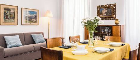 A dining area with a yellow table set for four, a sofa, and a cabinet with decorative items.