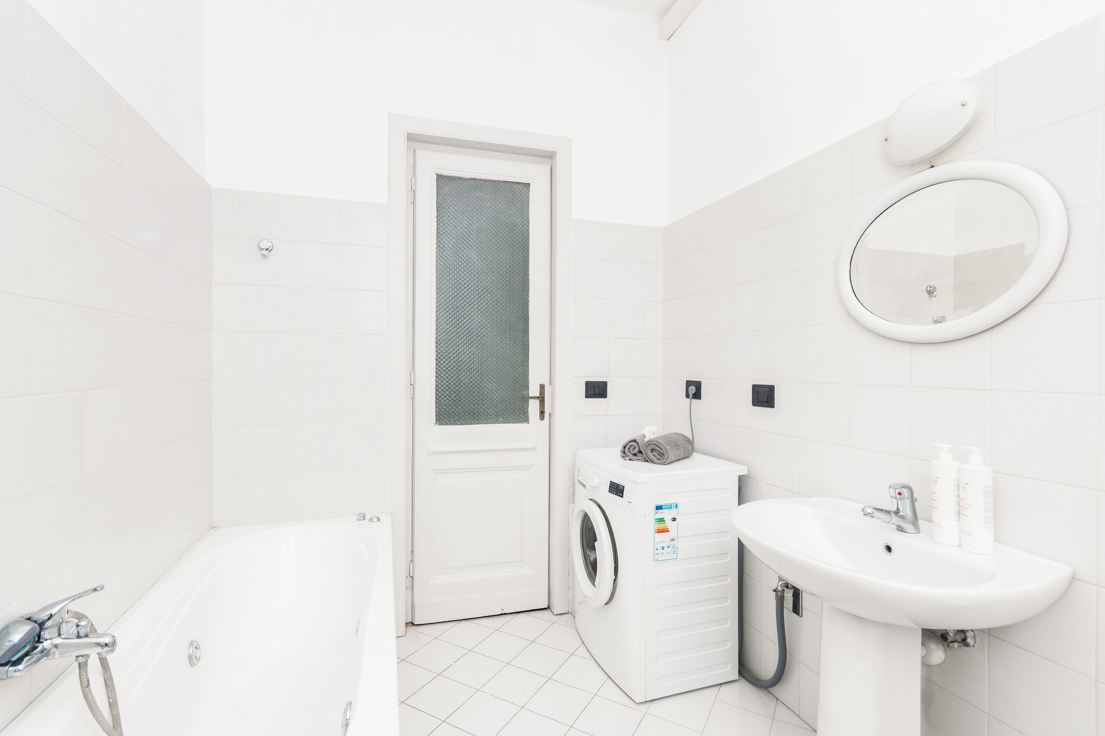 A modern bathroom with a white bathtub, a washing machine, and a sink.