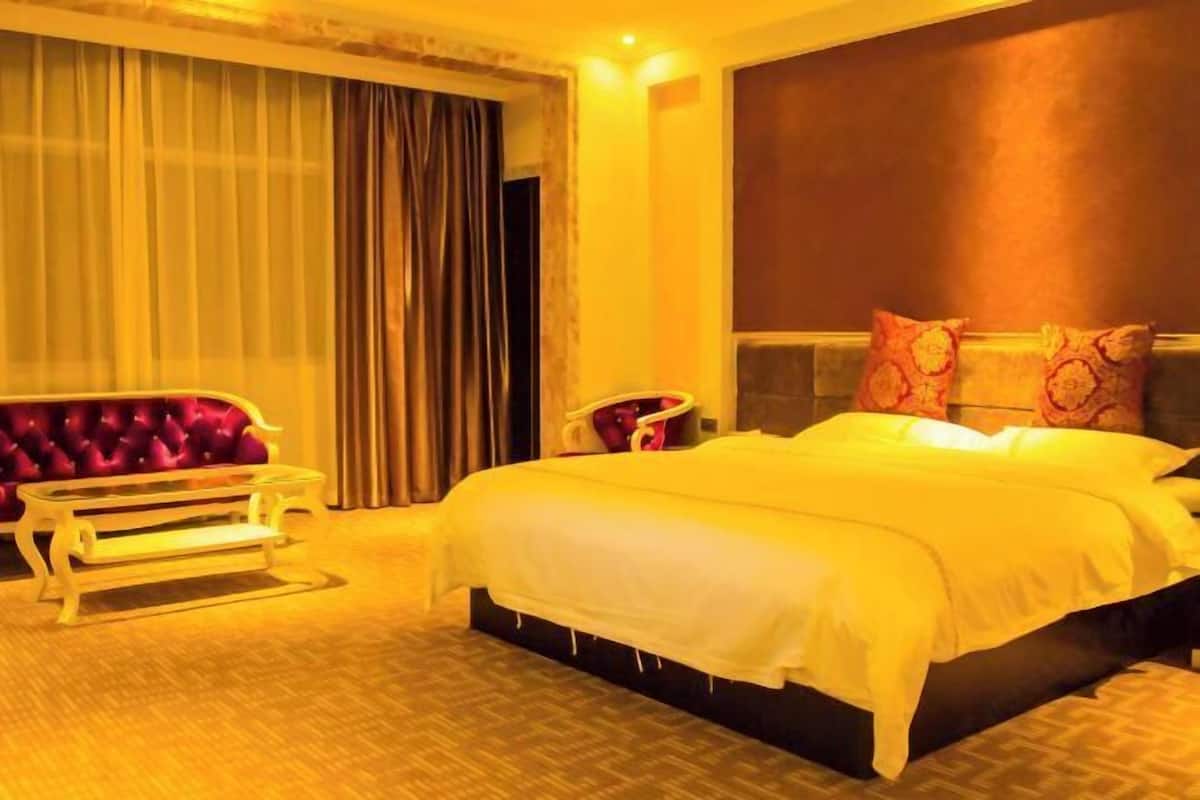 A hotel room with a large bed, a vanity with a mirror, and a seating area with a chair and a bench.