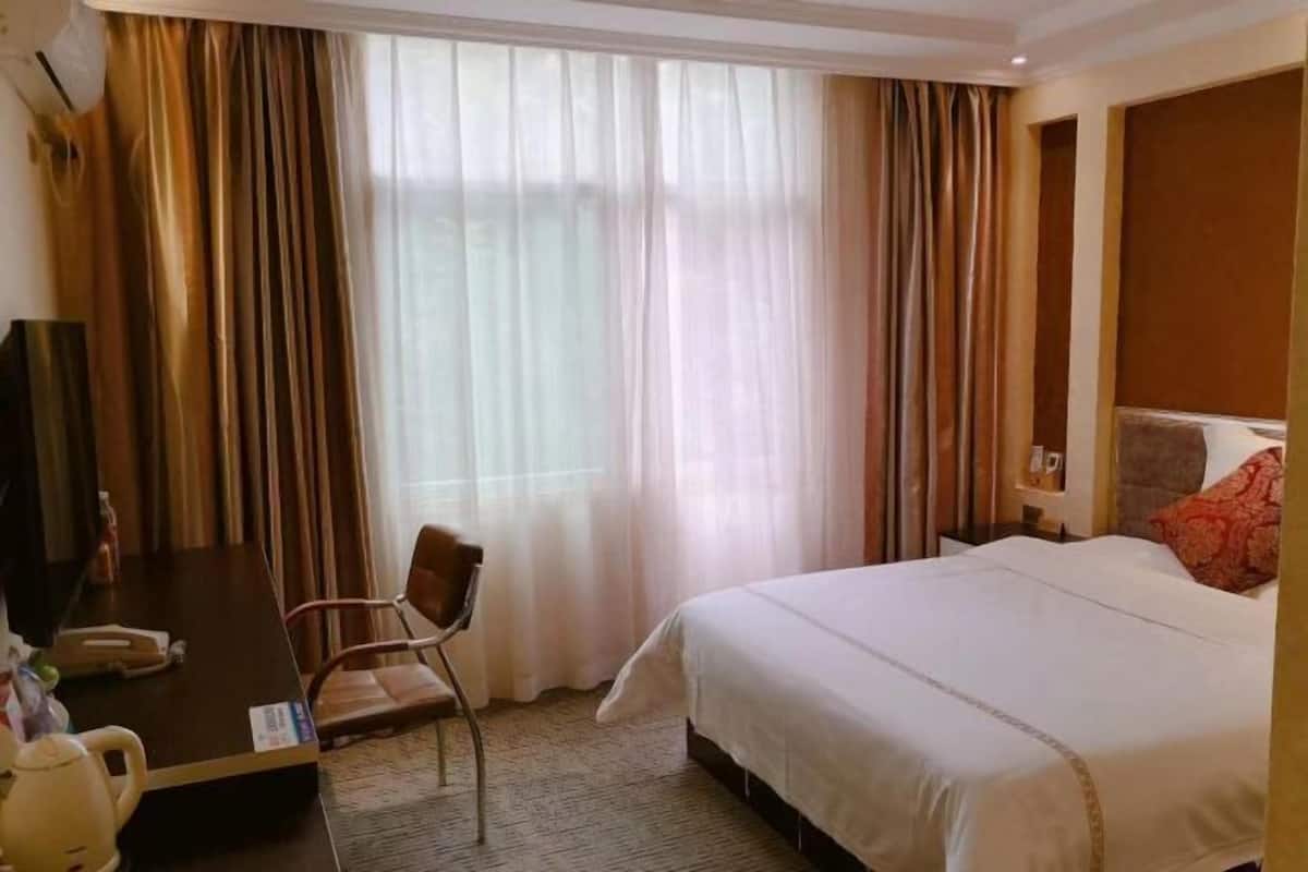 A hotel room with a bed, a desk, a chair, a television, and a window with curtains.