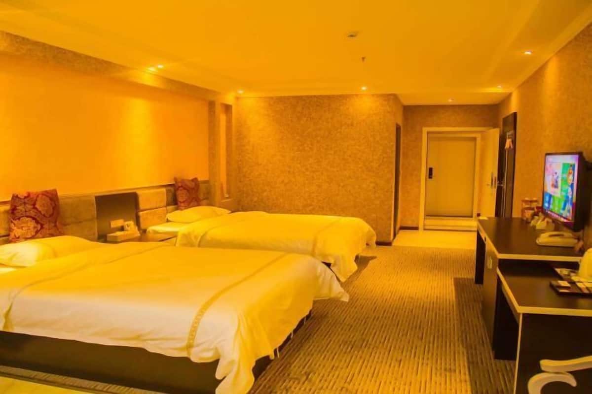 A hotel room with two beds, a desk, a television, and a door.