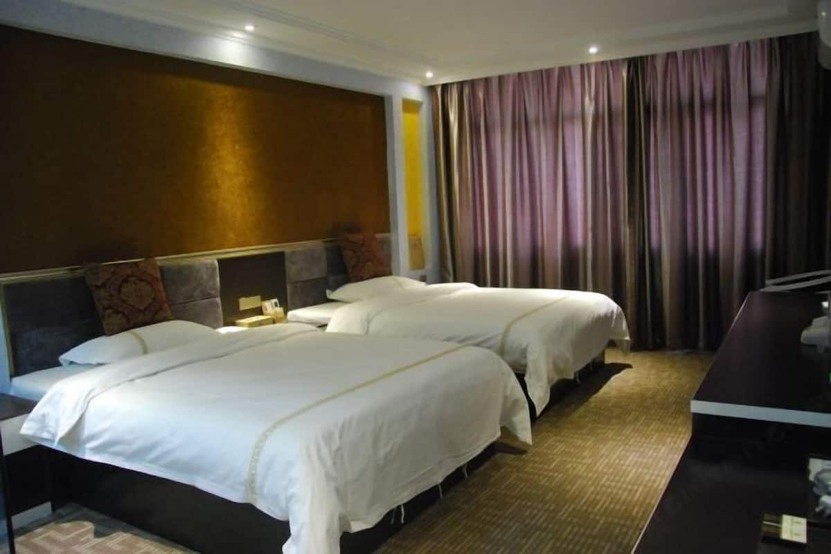 A hotel room with two beds, a desk, and a large window with curtains.