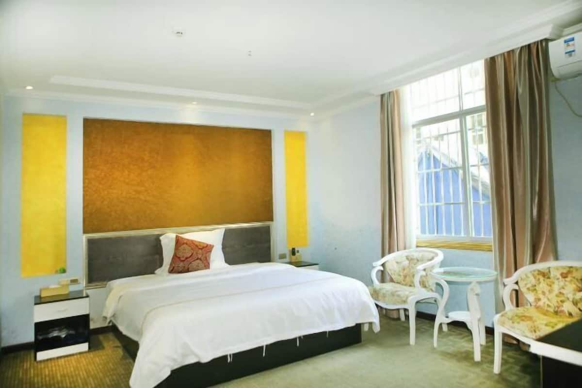 A hotel room with a bed, a chair, a small table, and a window with curtains.