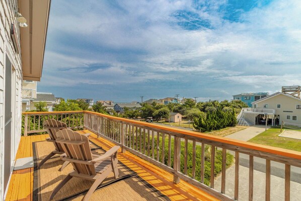 A balcony with wooden railings, a wooden deck, and two Adirondack chairs.