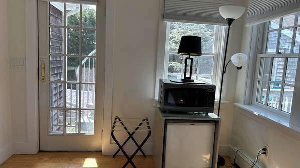 A room with a door leading to a balcony, a microwave on a glass shelf, a lamp, and a power outlet. - Ptown Paradise Farmhouse in the perfect, central location! (Provincetown)
