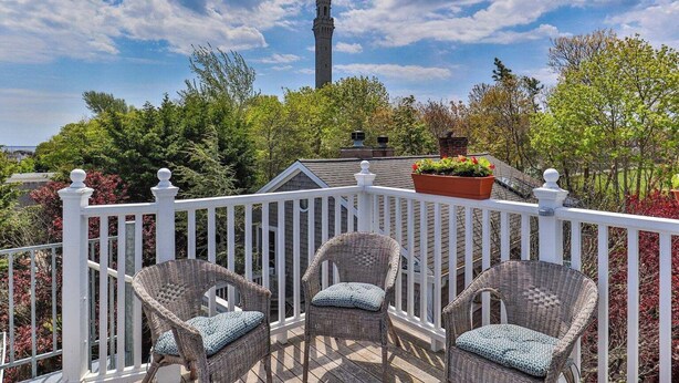 A balcony with wicker chairs and a white railing, overlooking a tower and lush greenery. - Ptown Paradise Farmhouse in the perfect, central location! (Provincetown)