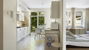 A modern, well-lit room with a bed, a small table, and a chair. There is a kitchen area with cabinets and a phone on the wall. - Elite Apartments Wesola Economy (Gdansk)