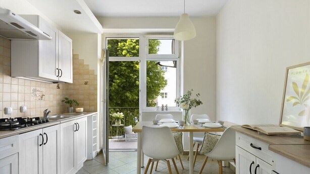 A modern kitchen with white cabinets, a dining area with a table and chairs, and a large window with a view of trees. - Elite Apartments Wesola Economy (Gdansk)
