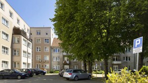 A parking area with multiple cars, a building with balconies, and a tree. - Elite Apartments Wesola Economy (Gdansk)