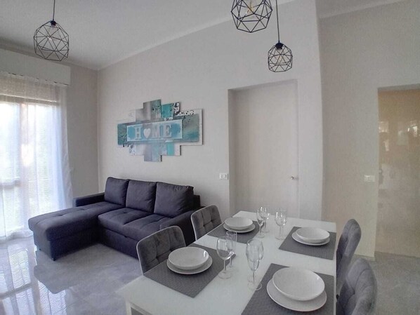 A modern living room with a grey sectional sofa, a dining table set with plates and glasses, and a wall art piece with the word "HOME". - New flat in the center of Viareggio (Viareggio)