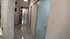 Um corredor com uma porta azul clara, uma luminária no teto e piso de azulejos.