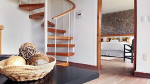 A modern interior with a spiral staircase, a stone wall, a bed, and a wicker basket on a table. - Eucaliptos Med Spa (Zitácuaro)