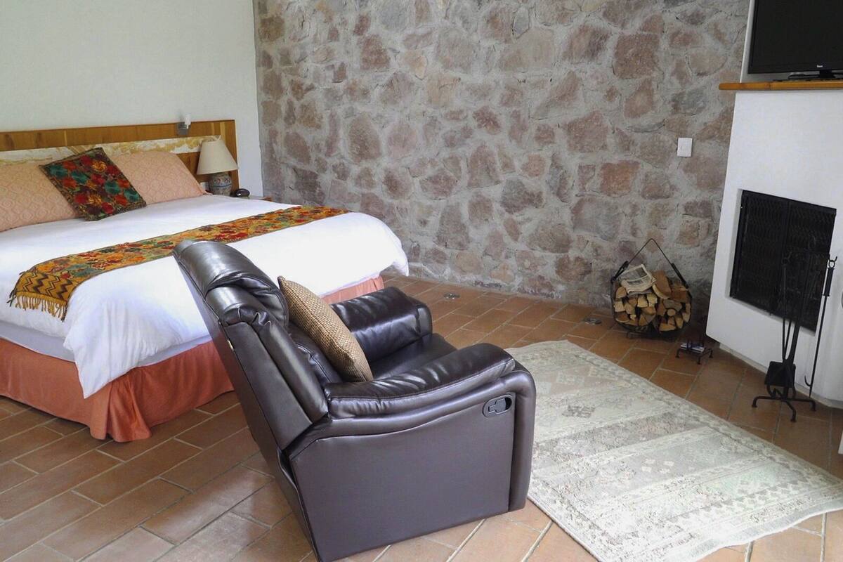 A bedroom with a bed, a massage chair, a stone wall, a fireplace, and a television.