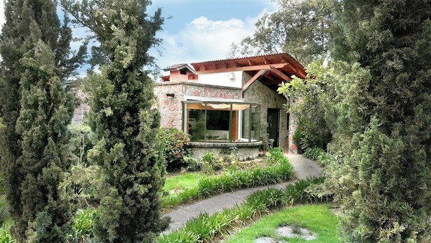 A rustic stone building with a glass conservatory, surrounded by dense greenery and a stone pathway. - Eucaliptos Med Spa (Zitácuaro)