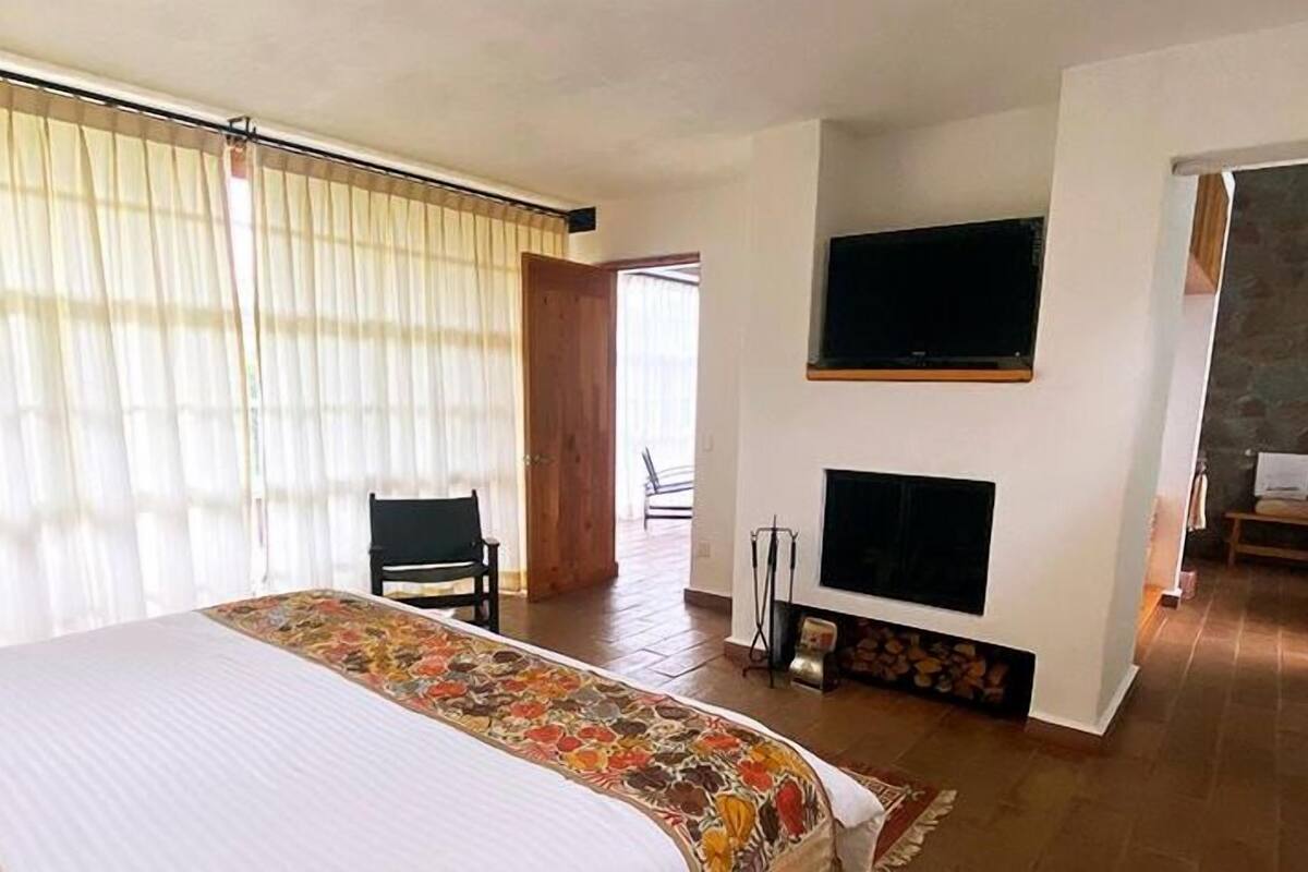 A hotel room with a bed, a TV mounted on the wall, a fireplace, and a bathroom visible through an open door.