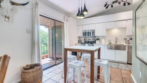 A modern kitchen with white cabinets, a stainless steel sink, and a dining area with a wooden table and white stools. - Downtown Treetop Hideaway- SXSW, 6th St, UT Campus

 (Austin)
