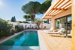 A pool area with wooden decking, lounge chairs, and a pergola.