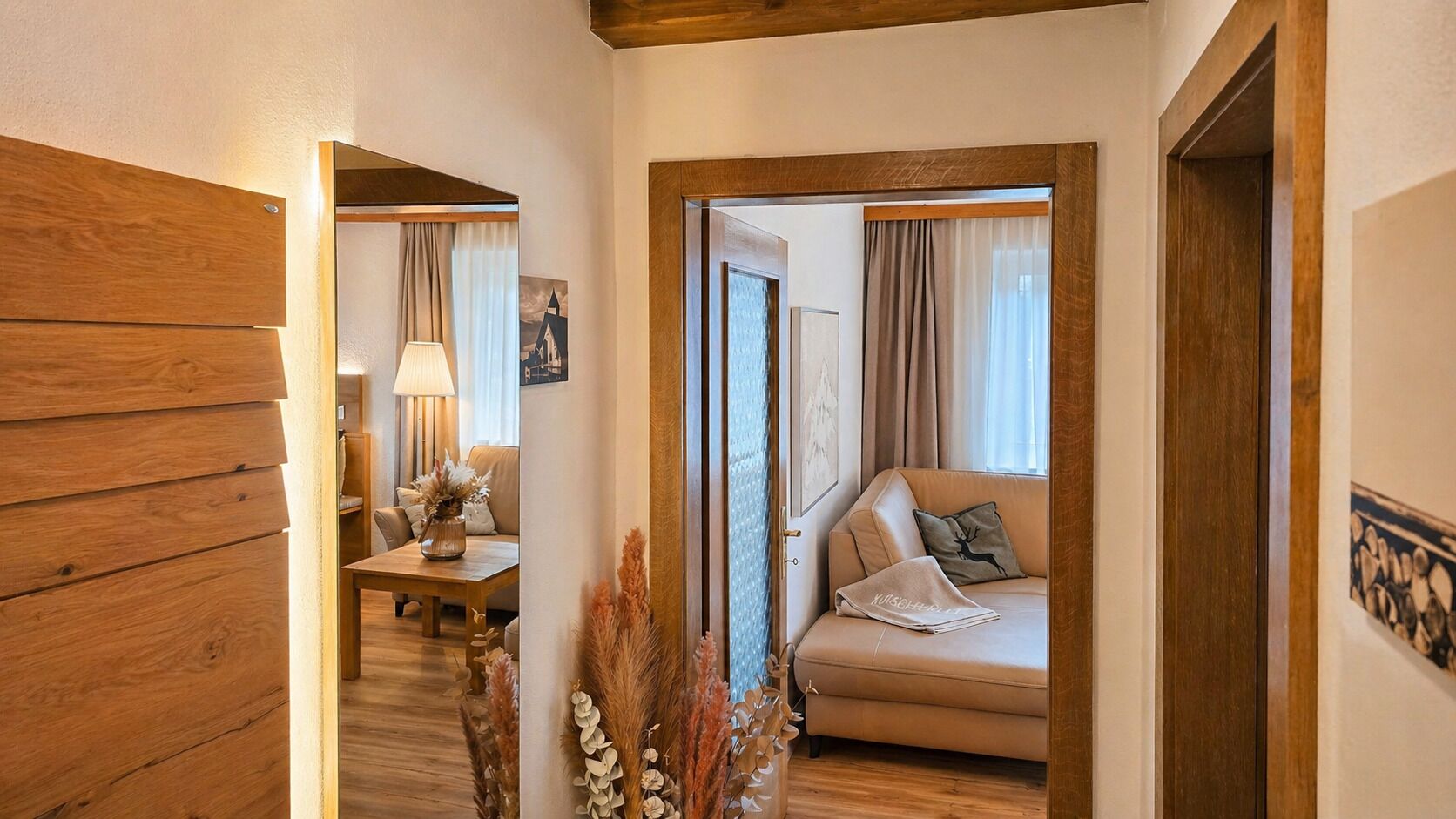 A hallway leading to a living area with a sofa, a lamp, and a vase with dried plants.