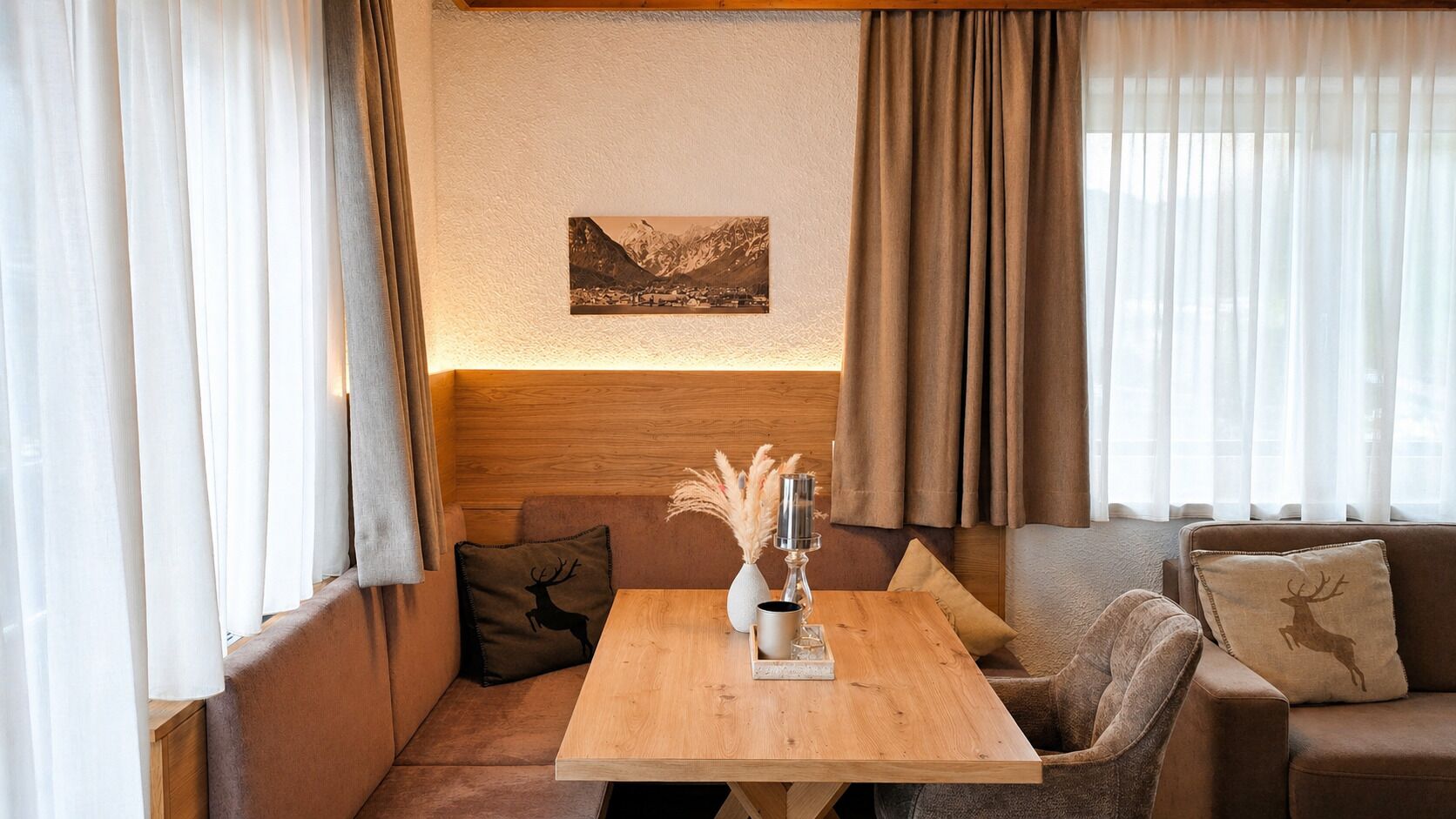 Una habitación acogedora con una mesa de madera, un sofá y un diván. Hay un cuadro en la pared y una ventana con cortinas.