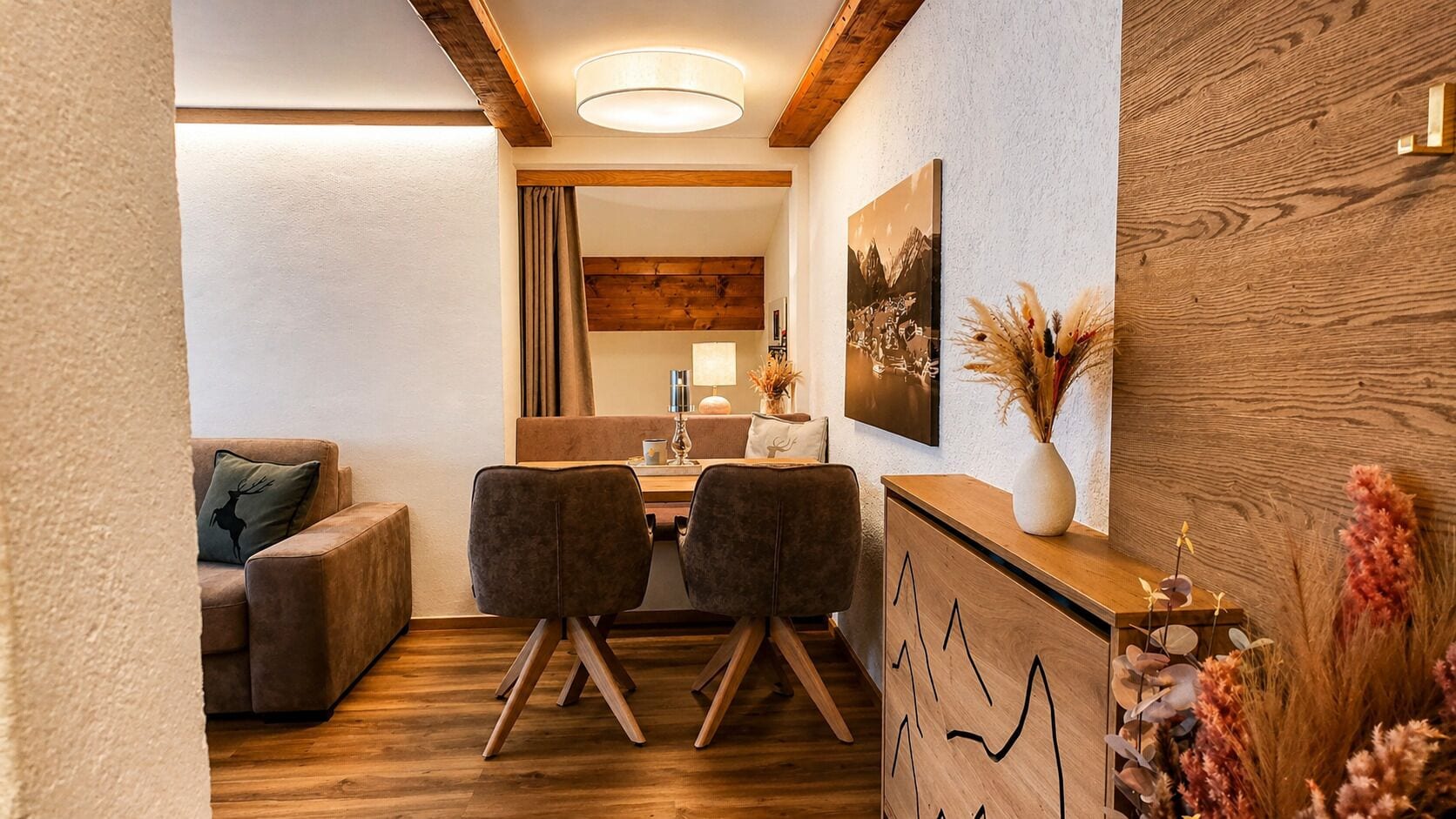 Una habitación acogedora con piso de madera, un sofá, dos sillones, un escritorio, una lámpara y un cuadro colgado en la pared.