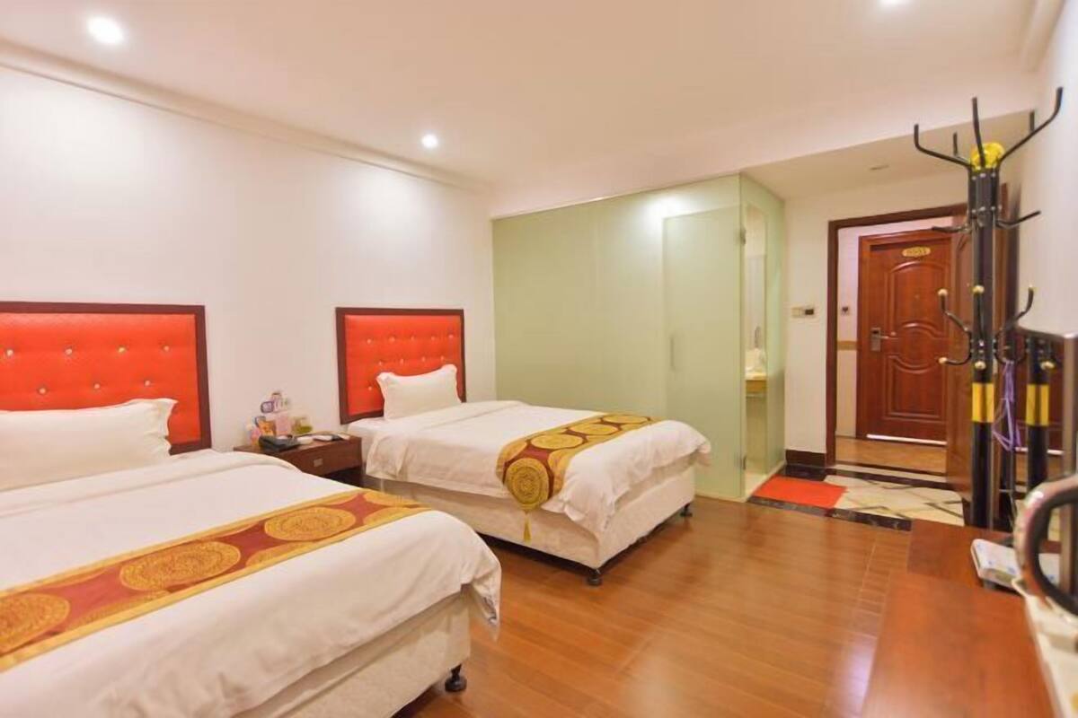 Une chambre d’hôtel avec deux lits, un plancher en bois, un porte-manteau et une porte.
