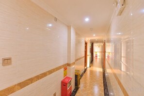 Un couloir d’hôtel avec un sol en marbre, une boîte aux lettres rouge et une porte au bout.
