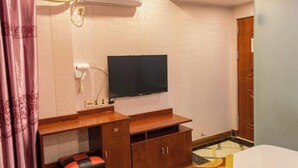 Een hotelkamer met een wandgemonteerde flatscreen televisie, een houten tv-meubel, een bed met een beddengoed met een patroon, en een betegelde vloer.