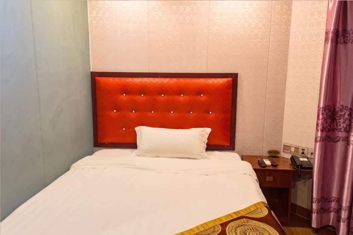 Une chambre d’hôtel avec une tête de lit rouge, une couvre-lit blanche, une table de chevet avec une lampe et un téléphone.