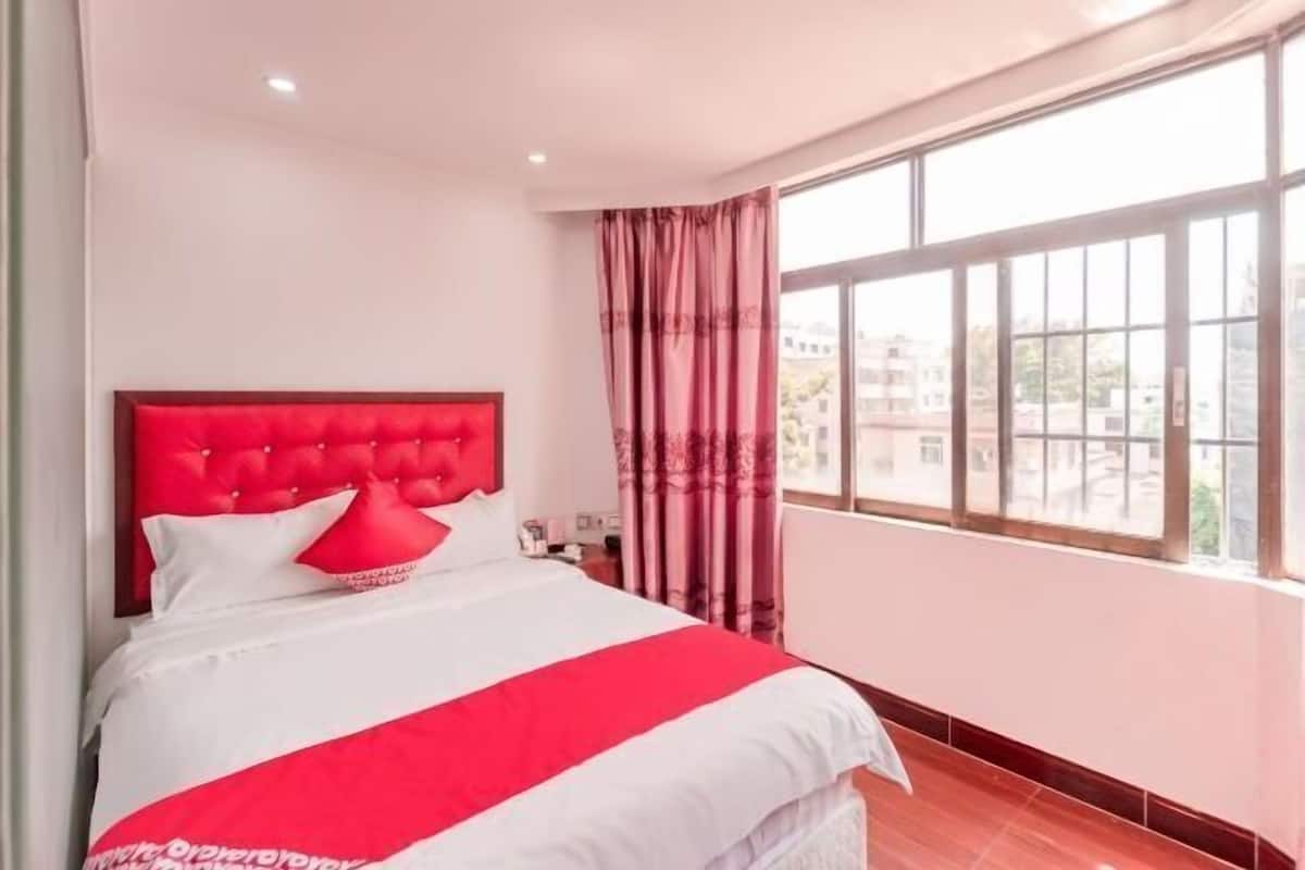 Une chambre d’hôtel avec un grand lit, une fenêtre avec des rideaux et une vue sur les bâtiments environnants.