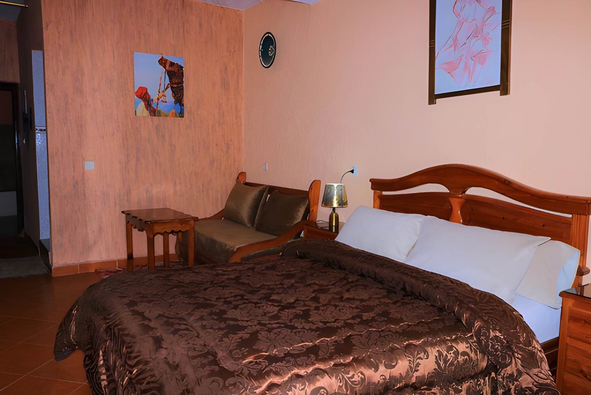 A bedroom with a large bed, a wooden headboard, a nightstand, a lamp, and a painting on the wall.