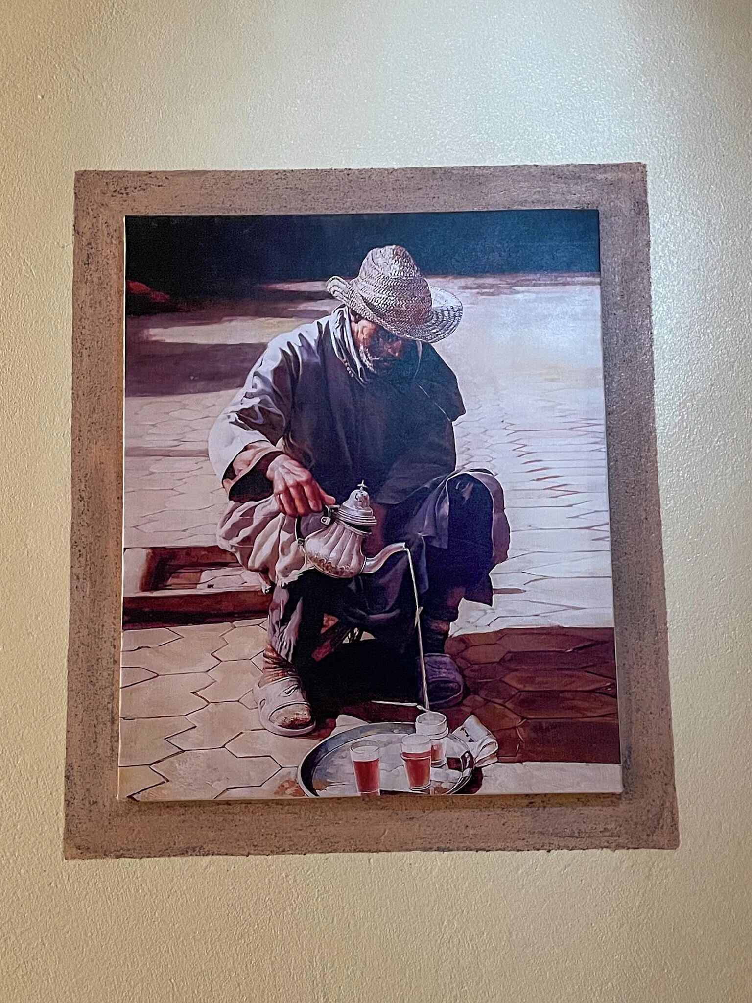 Un tableau encadré représentant une personne assise par terre, avec une théière et des tasses.