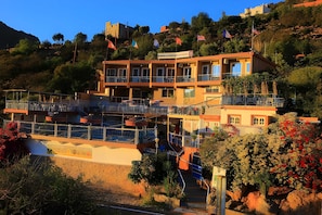 Un hôtel à plusieurs étages, doté de balcons, situé sur une colline et orné de drapeaux.