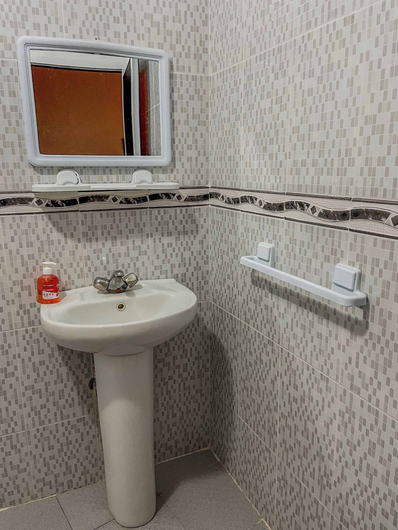Ett badrum med ett vitt handfat, en spegel och en tvåldispenser.