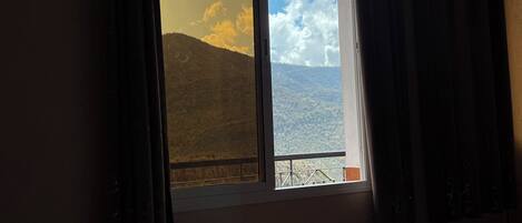 Habitación de hotel con un amplio ventanal que ofrece vistas a un paisaje montañoso.