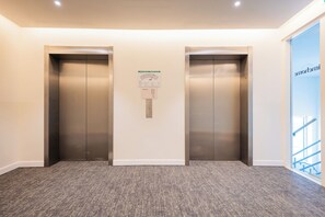 Un área de ascensores moderna con dos ascensores y un cartel con el plano de la planta en la pared.
