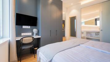 Un dormitorio moderno con cama, escritorio, silla, televisor y un espejo grande.