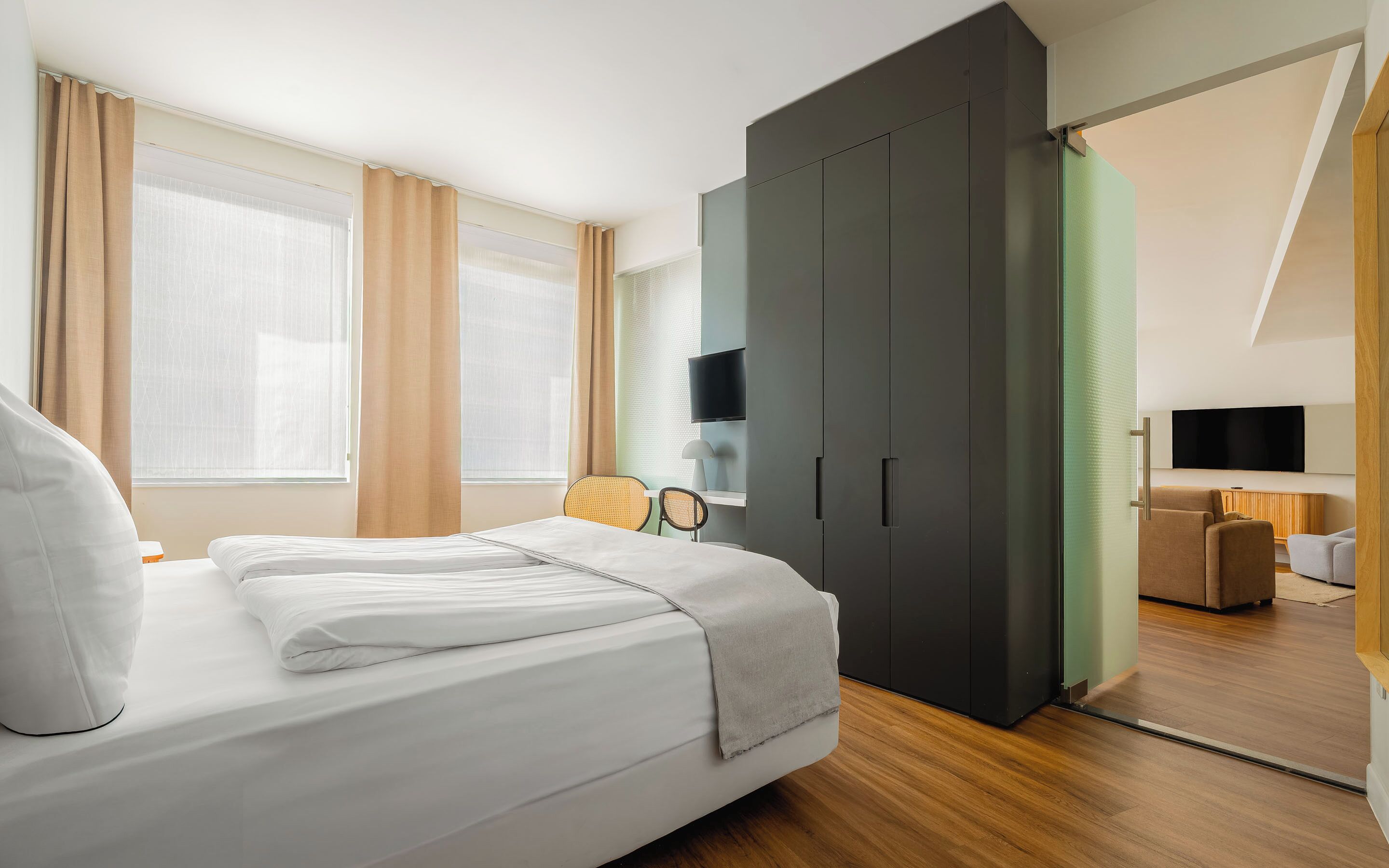 Ein modernes Hotelzimmer mit einem Bett, einem Schreibtisch, einem Sessel, einem Kleiderschrank und einem Fernseher.