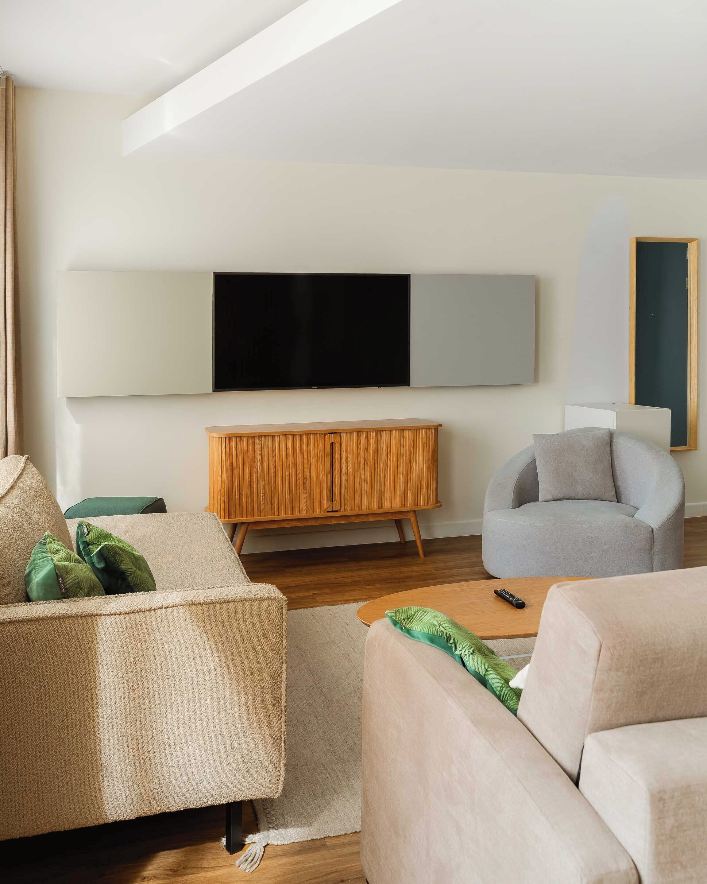 Un salon moderne avec un téléviseur à écran plat, un meuble en bois et deux canapés.