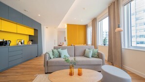 A modern living room with a sofa, a coffee table, and a kitchen area with yellow cabinets. - Limehome Amsterdam Westerpark (Amsterdam)