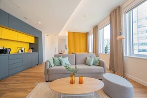 A modern living room with a sofa, a coffee table, and a kitchen area with yellow cabinets. - Limehome Amsterdam Westerpark (Amsterdam)