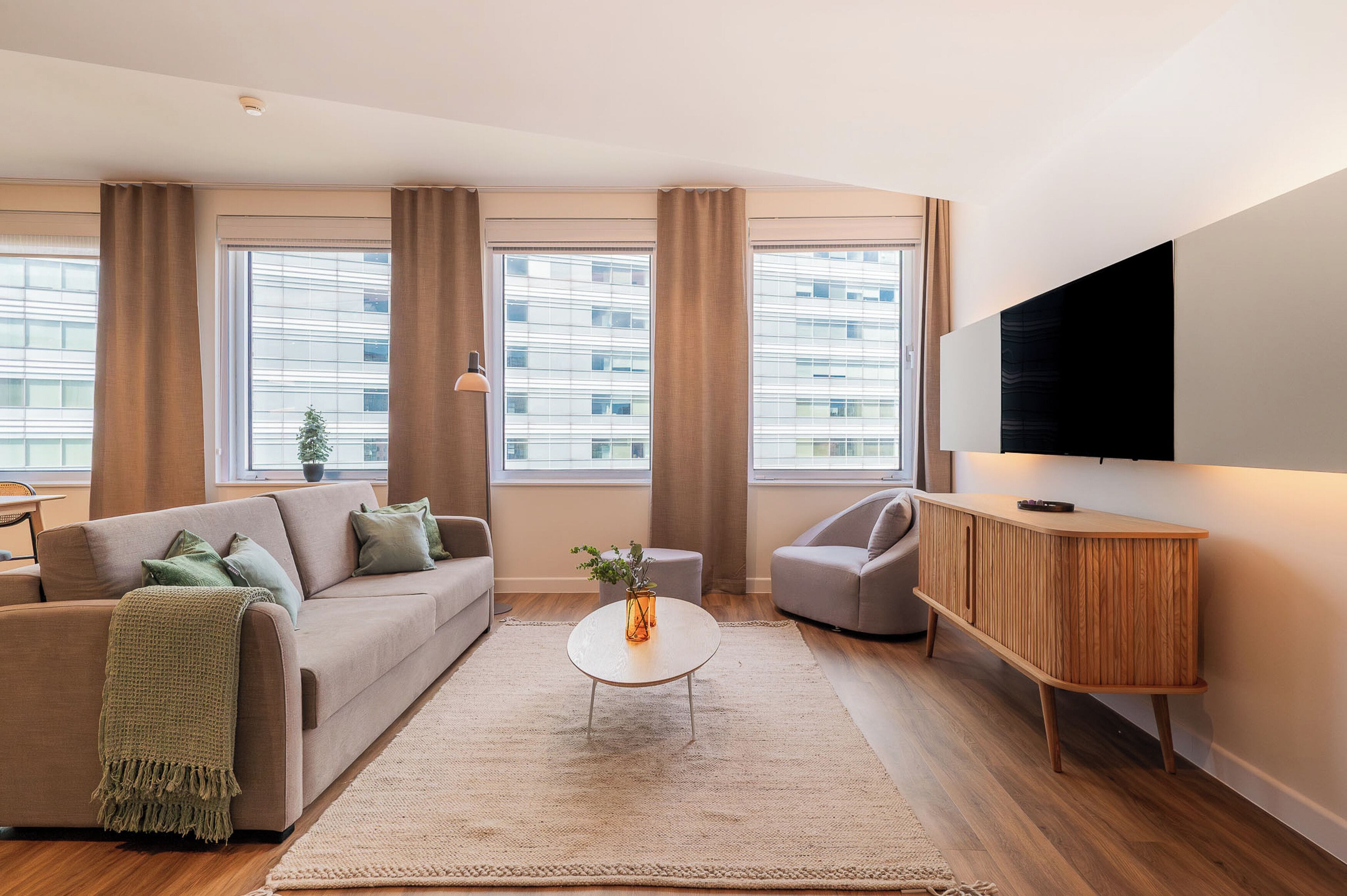 A modern living room with a sofa, armchair, coffee table, and a TV mounted on the wall.
