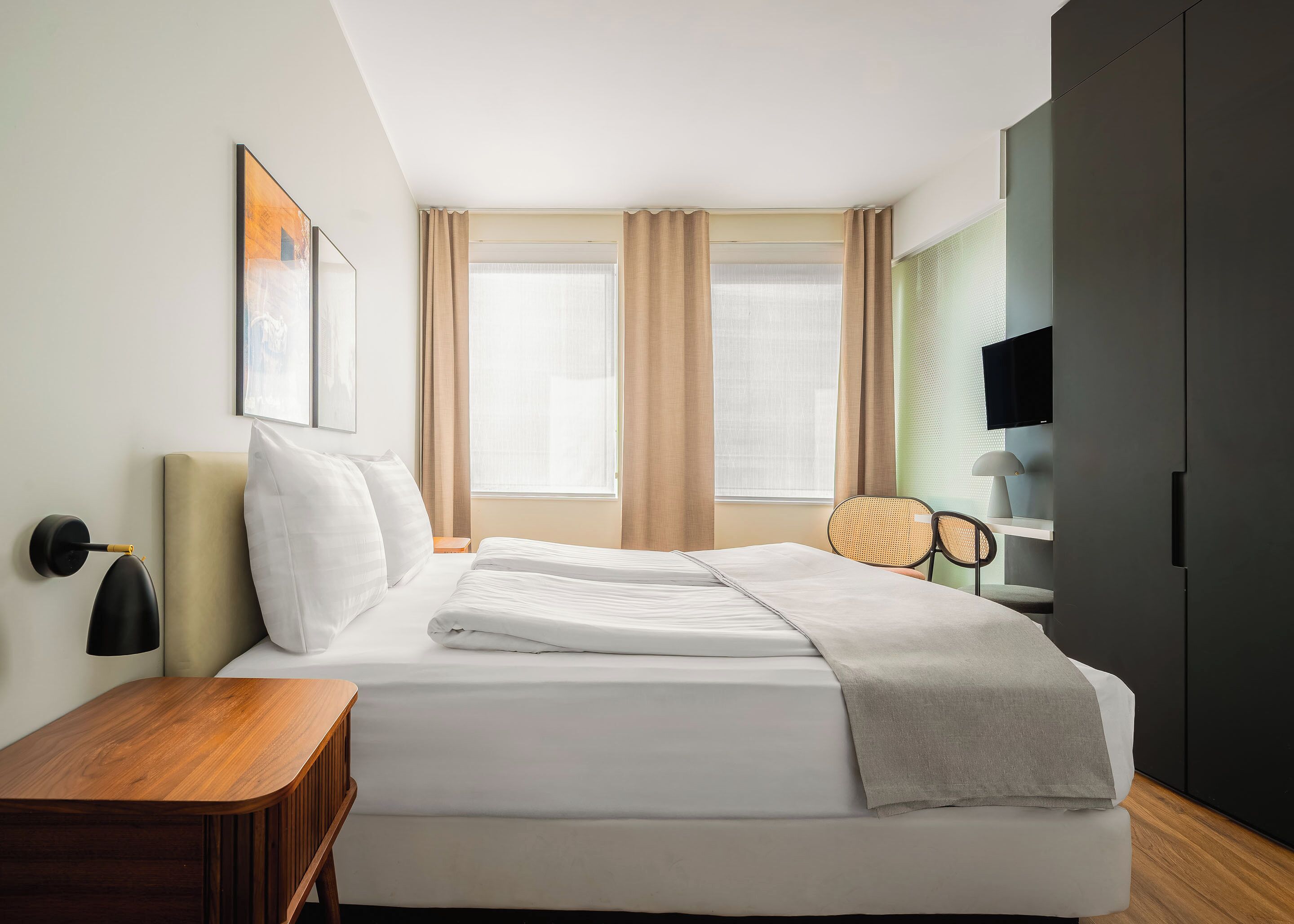 A hotel room with a bed, bedside table, chair, TV, and curtains.