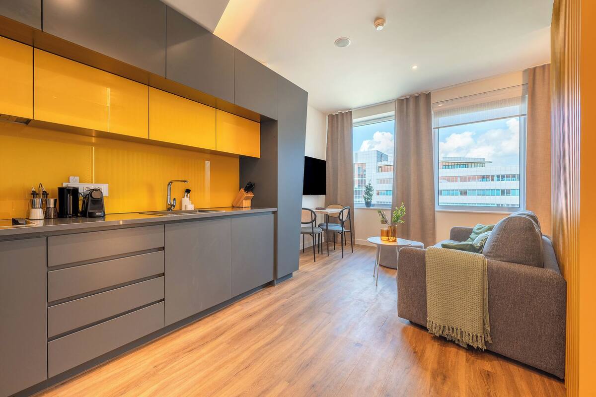 Una cocina moderna con armarios grises y encimera de madera, un comedor con mesa y sillas, y un sofá con una manta.